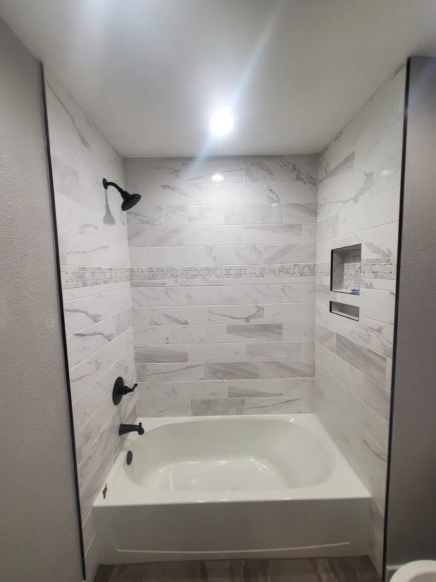 A finished bathroom remodel by Coyt Handyman Services, marble-pattern tile with bronze fixtures.